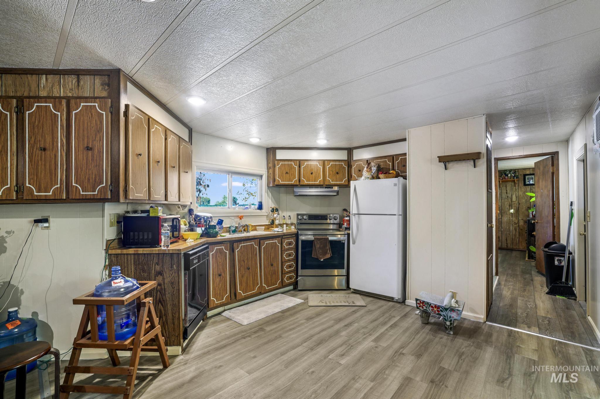 Kitchen with freestanding refrigerator, stainless steel electric range, light wood-type flooring, a textured ceiling, and black dishwasher