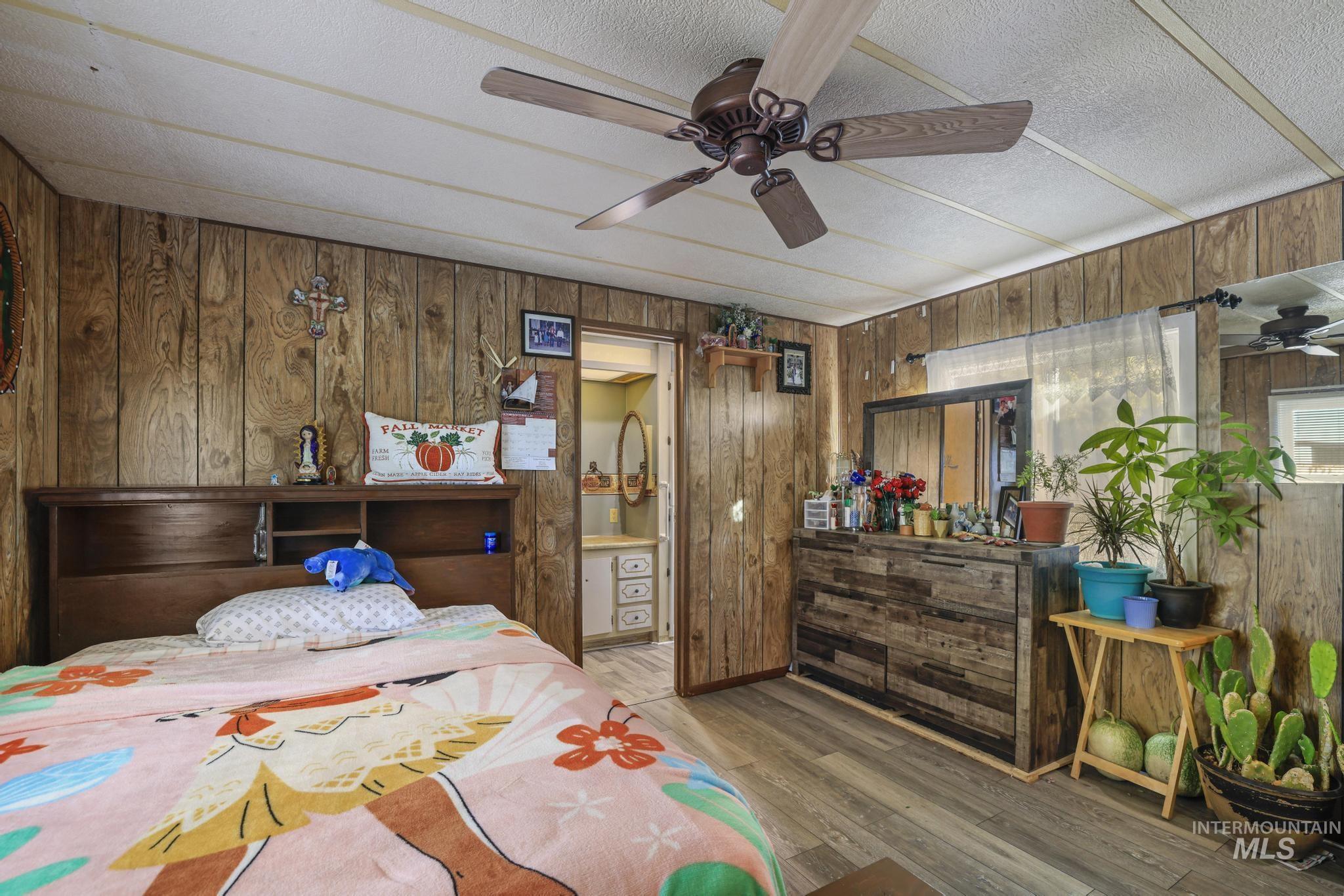 Bedroom with wood walls, wood finished floors, and a ceiling fan