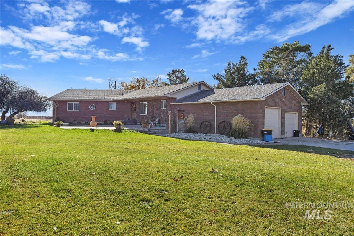 Rear view of property with a yard, brick siding, a garage, and concrete driveway