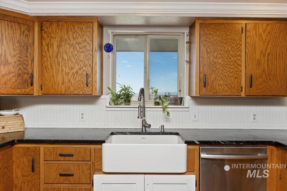 Kitchen with brown cabinets, dishwasher, and dark stone countertops