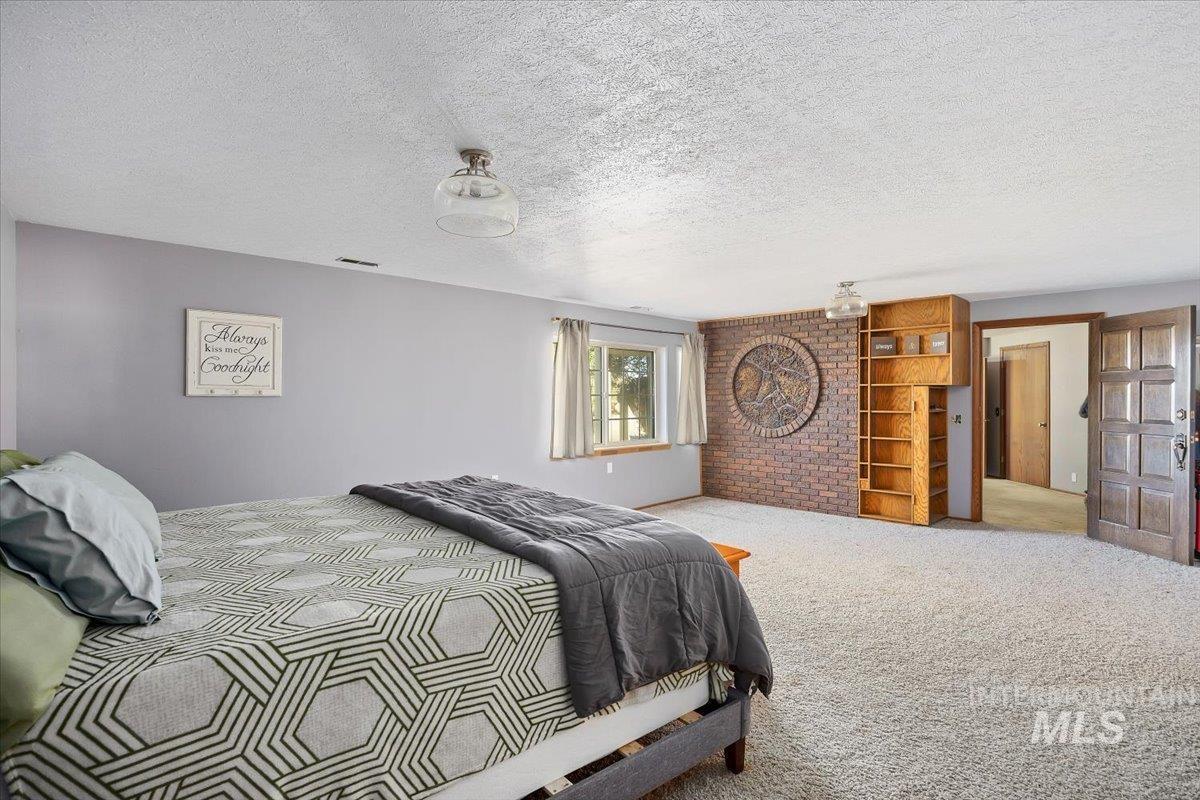 Carpeted bedroom featuring a textured ceiling and brick wall