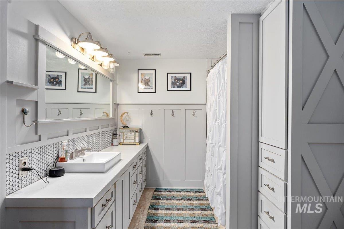 Bathroom with vanity, curtained shower, a wainscoted wall, and backsplash