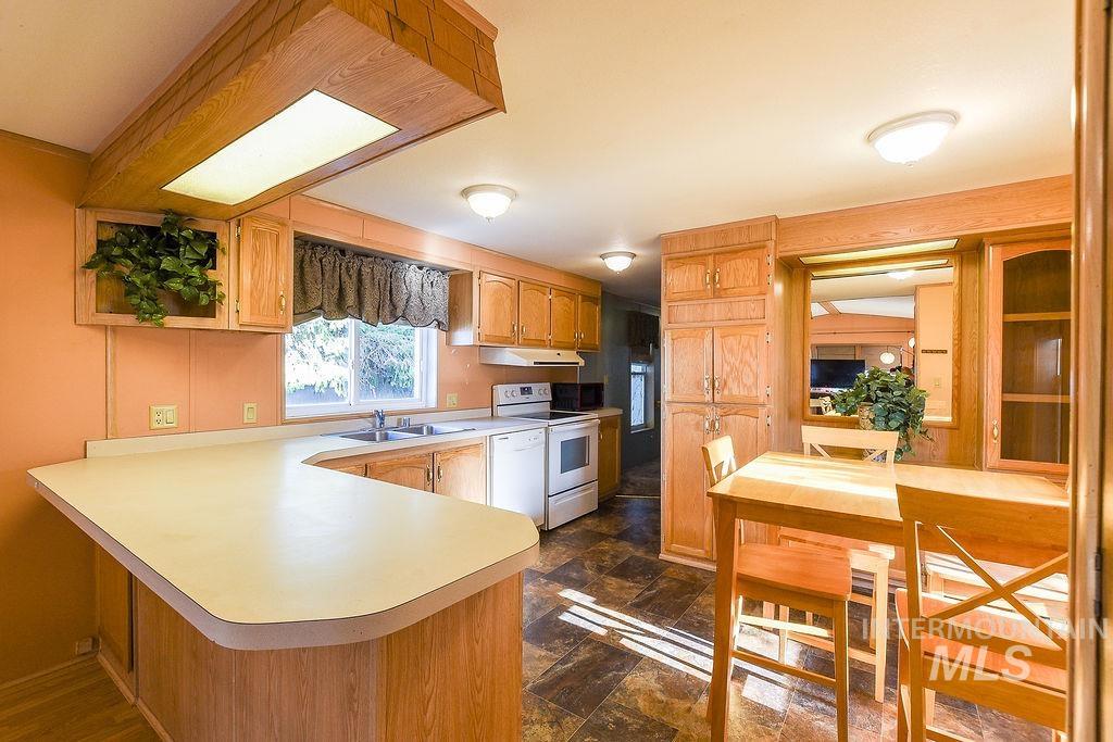 Kitchen with light countertops, a peninsula, white appliances, dark stone finish floors, and brown cabinetry