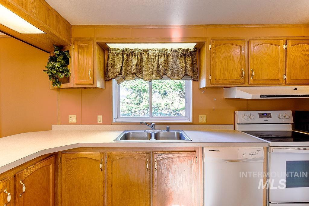 Kitchen featuring white appliances, light countertops, extractor fan, and brown cabinetry