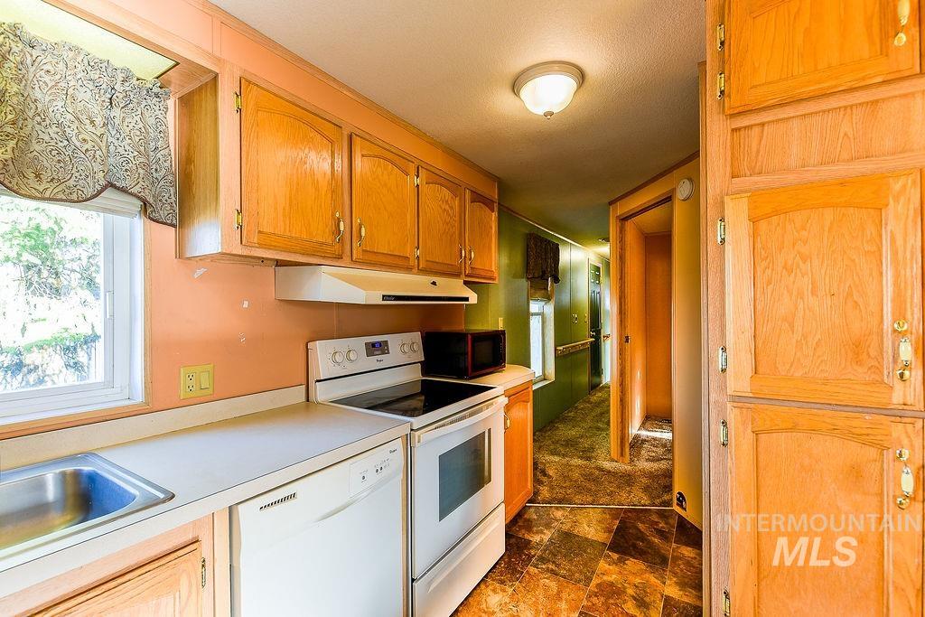 Kitchen with white appliances, light countertops, stone finish flooring, and under cabinet range hood