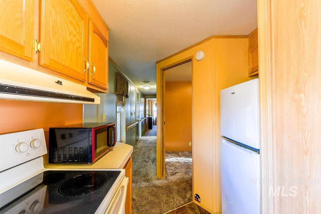 Kitchen with white appliances, dark colored carpet, under cabinet range hood, and a textured ceiling
