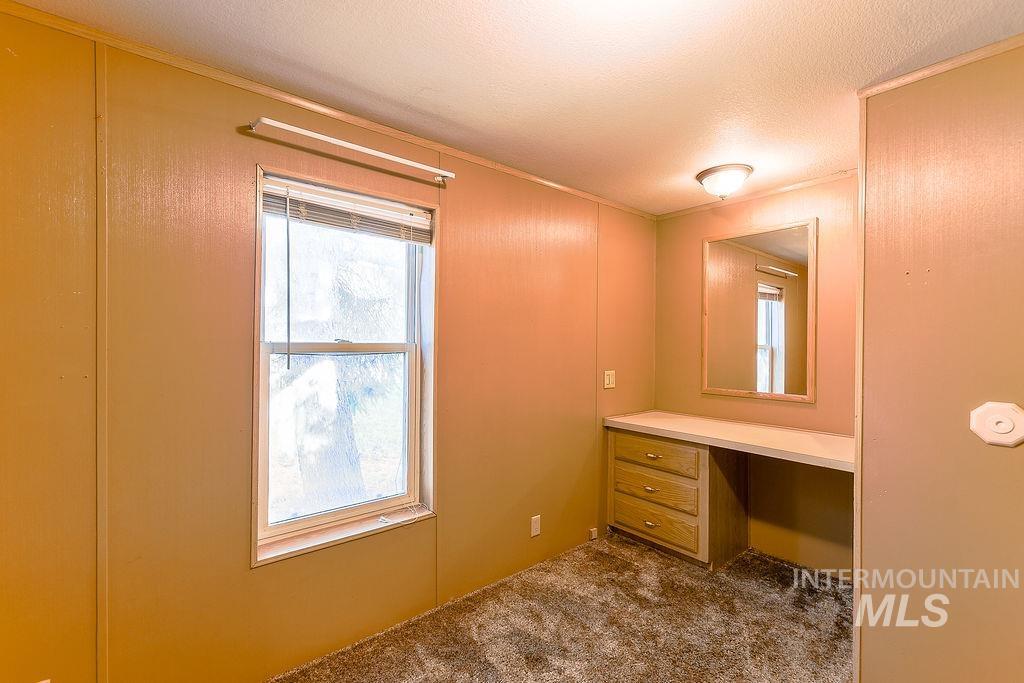 Unfurnished office featuring built in desk, dark colored carpet, plenty of natural light, a textured ceiling, and ornamental molding
