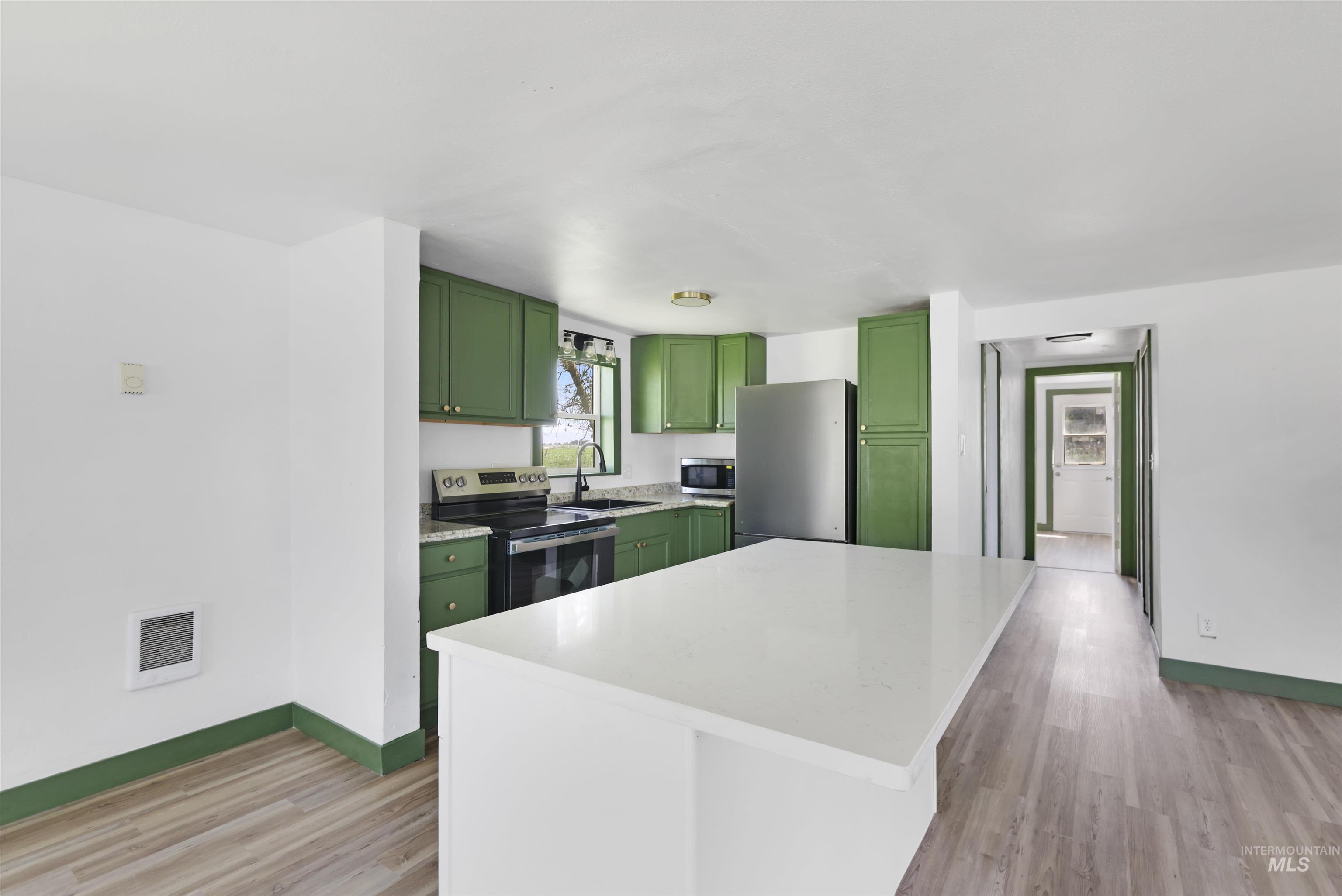 Kitchen featuring green cabinets, stainless steel appliances, light wood-style flooring, and a center island
