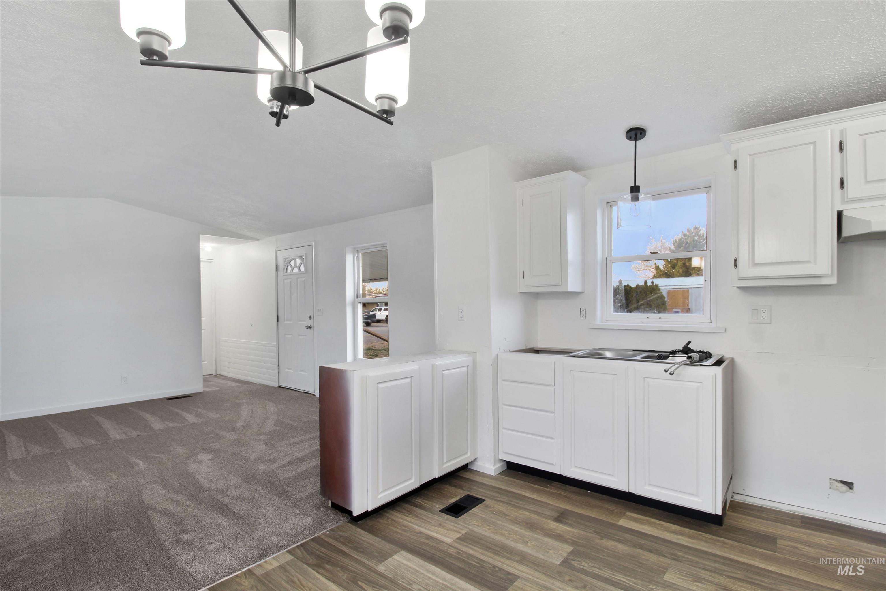 Kitchen featuring hanging light fixtures, white cabinets, dark wood-type flooring, light countertops, and a chandelier