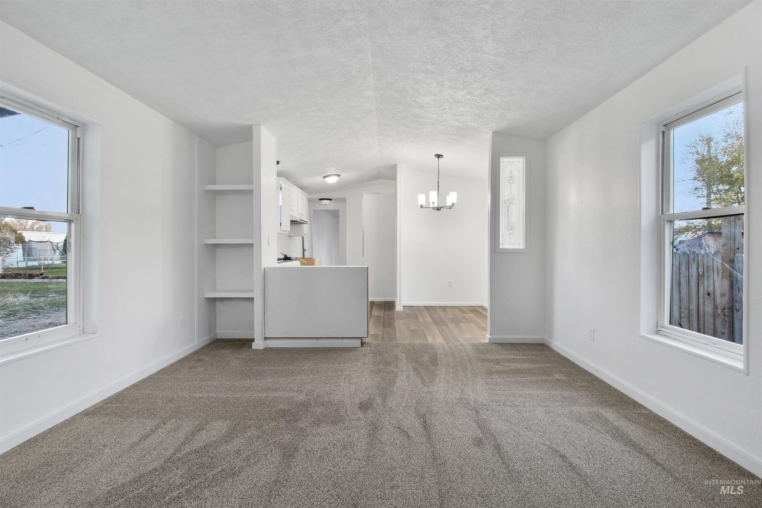 Unfurnished living room with dark colored carpet, a textured ceiling, a chandelier, and built in shelves