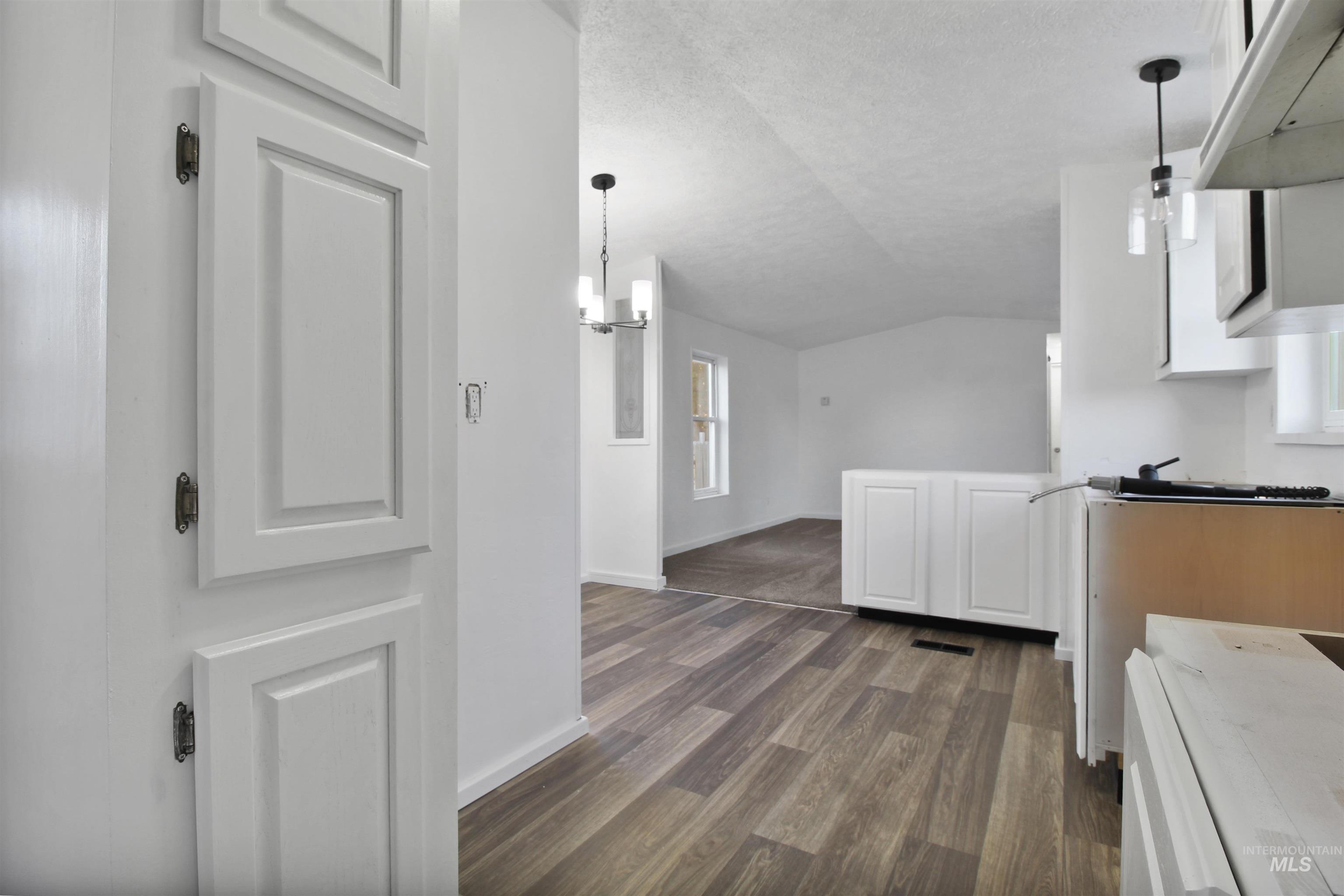 Kitchen with lofted ceiling, white cabinetry, white stove, pendant lighting, and a textured ceiling