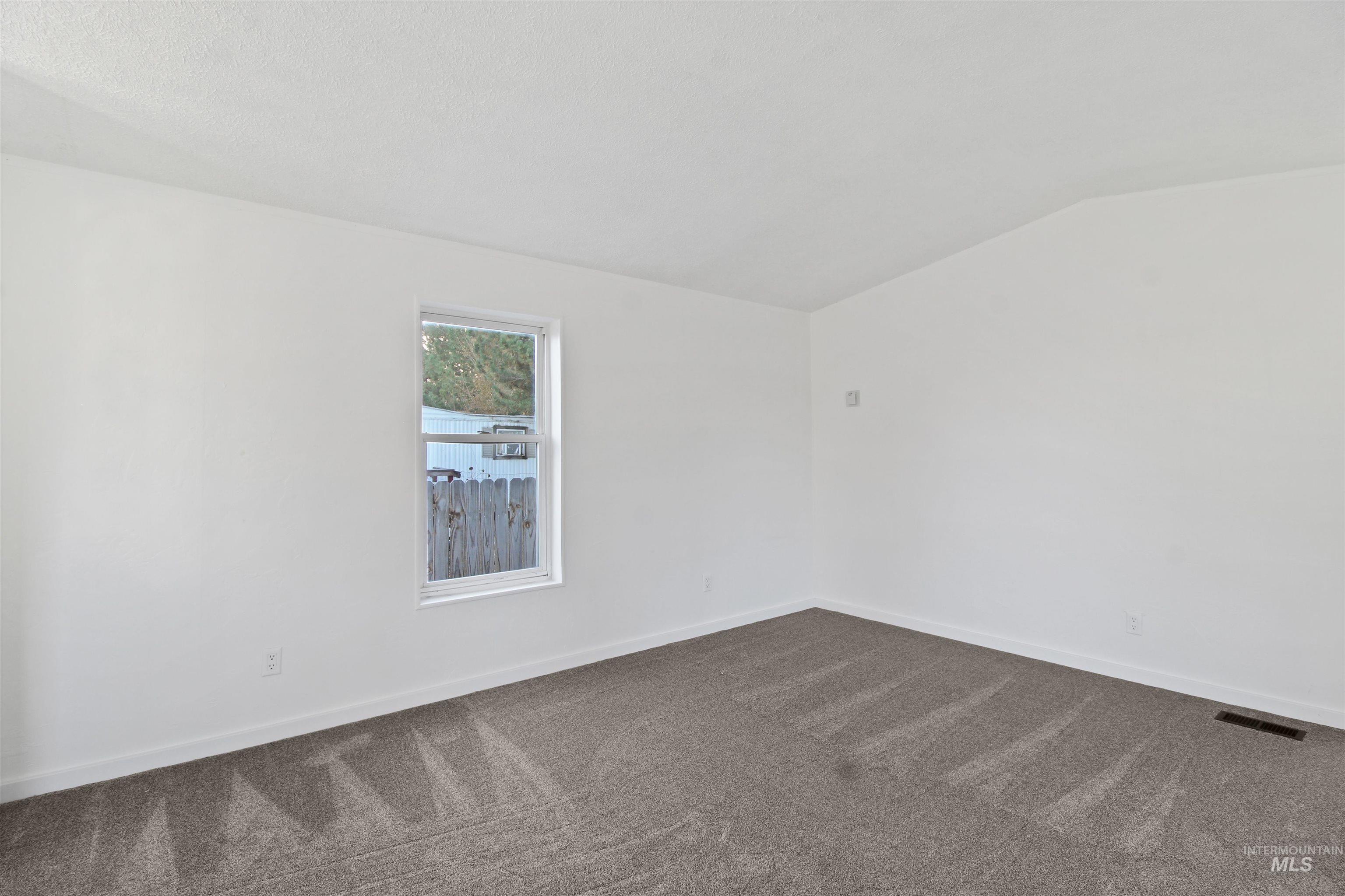 Empty room with dark carpet and vaulted ceiling