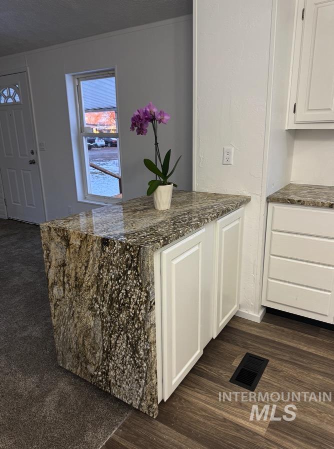 Kitchen with dark stone countertops, white cabinets, a peninsula, dark wood-style flooring, and a textured ceiling
