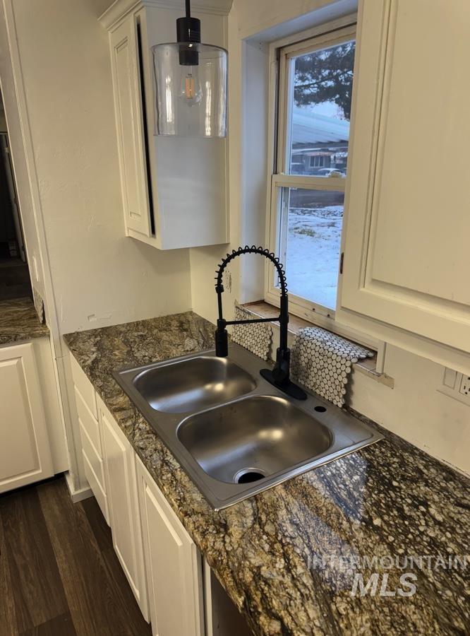 Kitchen view of white cabinetry, hanging light fixtures, dark wood-style floors, and dark stone countertops