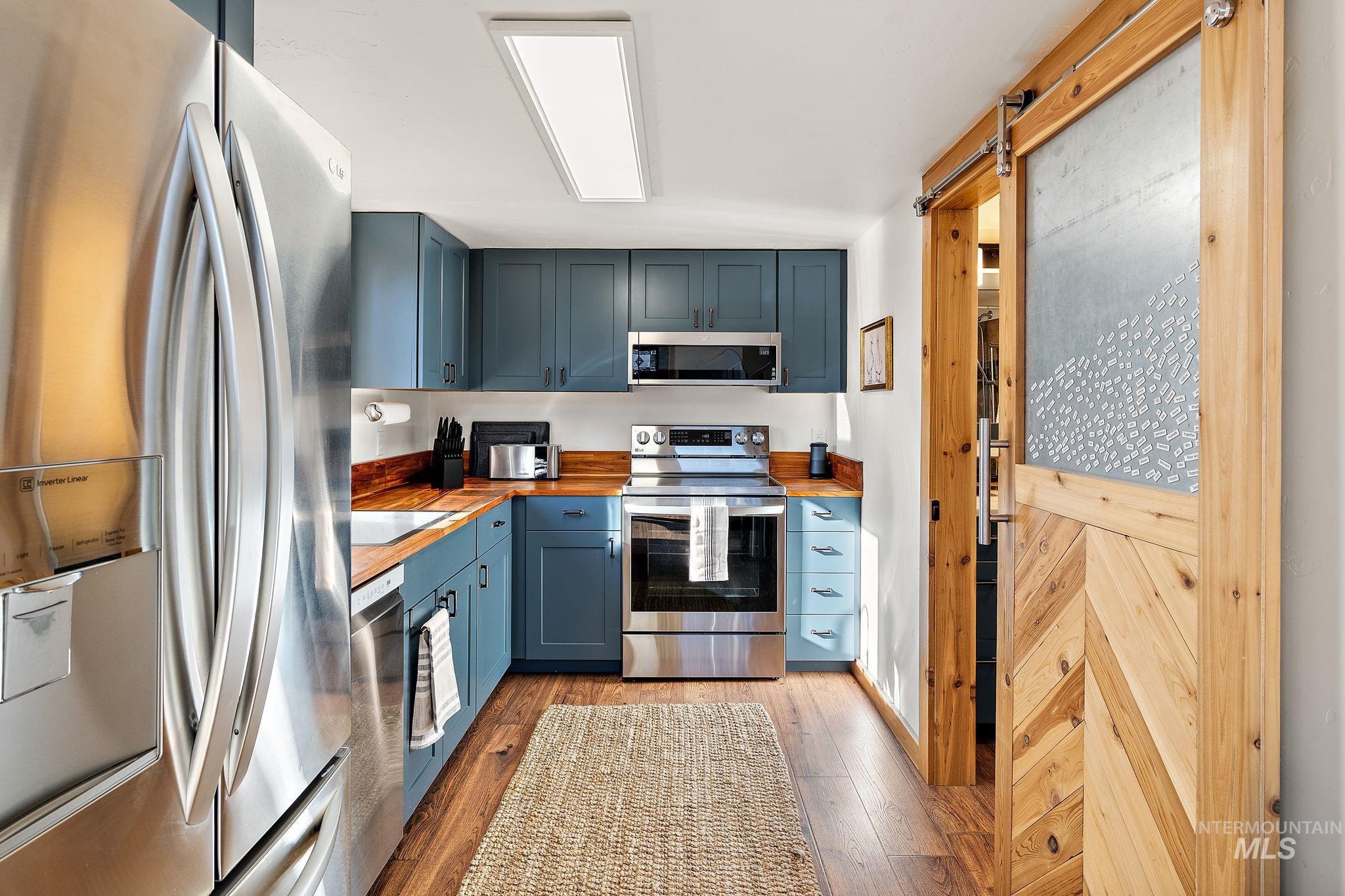 Kitchen featuring a barn door, butcher block counters, appliances with stainless steel finishes, dark wood-style floors, and blue cabinets