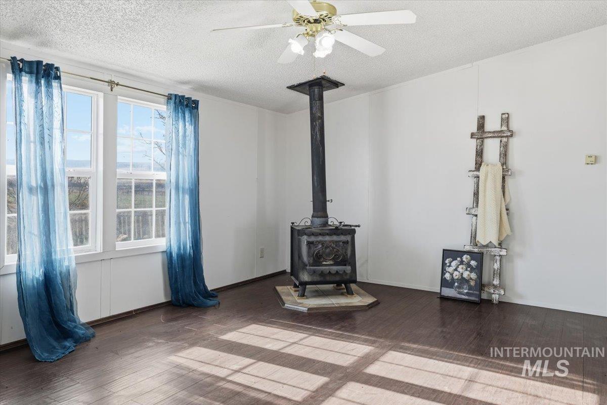 Unfurnished living room with a wood stove, wood finished floors, a textured ceiling, and ceiling fan
