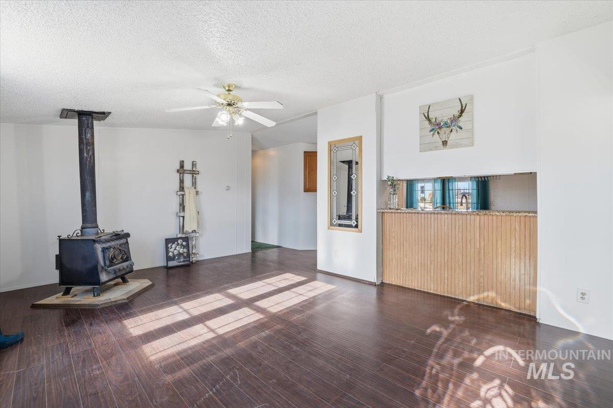 Unfurnished living room with a wood stove, dark wood finished floors, a textured ceiling, and a ceiling fan