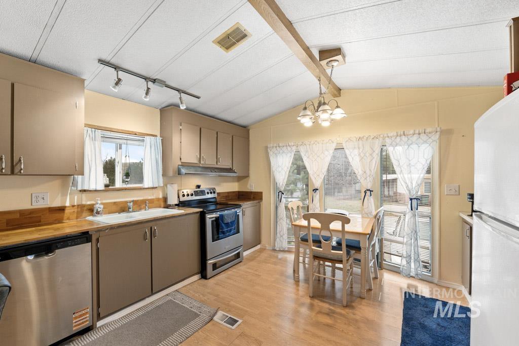 Kitchen with lofted ceiling, appliances with stainless steel finishes, gray cabinets, light wood-style flooring, and a chandelier