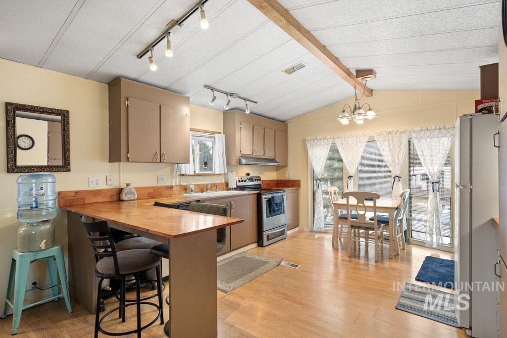 Kitchen featuring wooden counters, stainless steel range with electric stovetop, a peninsula, freestanding refrigerator, and a breakfast bar
