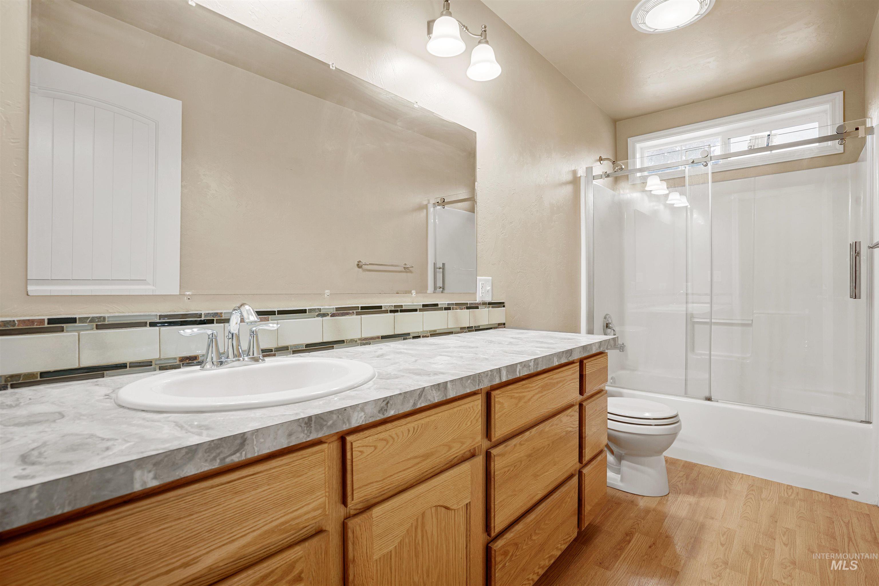 Full bathroom with vanity, bath / shower combo with glass door, light wood-type flooring, and decorative backsplash