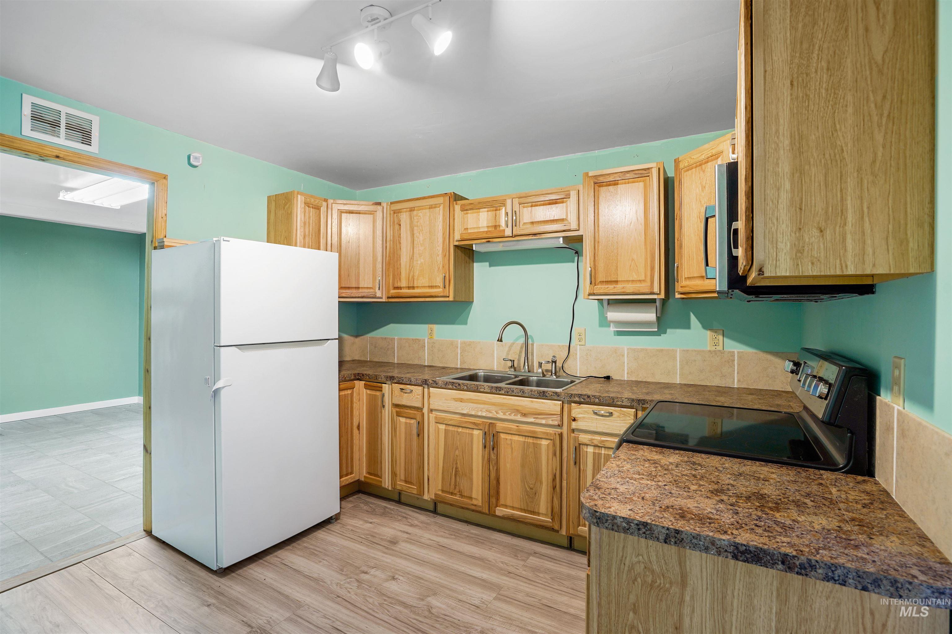 Kitchen featuring freestanding refrigerator, electric range, light wood finished floors, and dark countertops