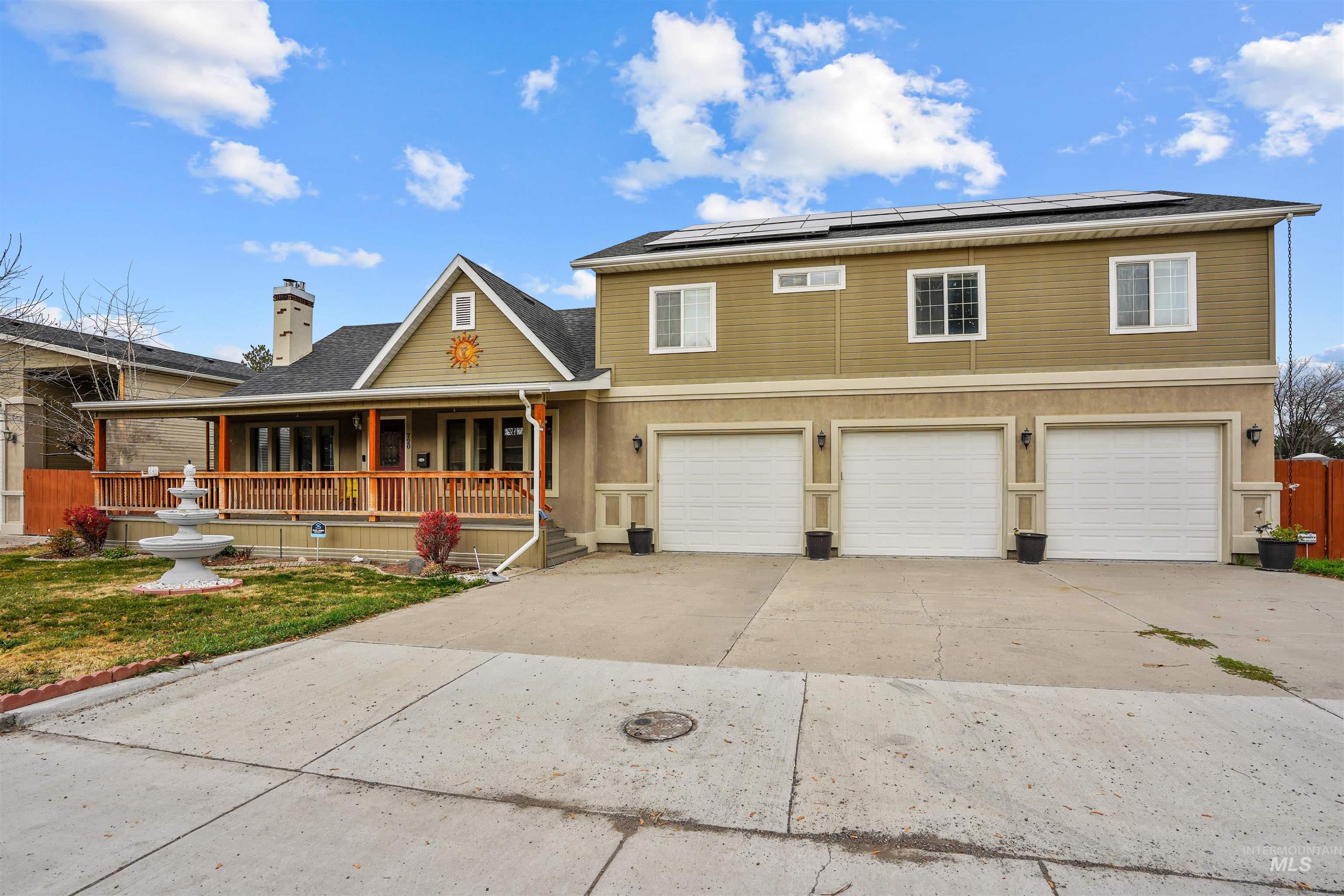 View of front of home featuring a porch, concrete driveway, roof mounted solar panels, a chimney, and an attached garage