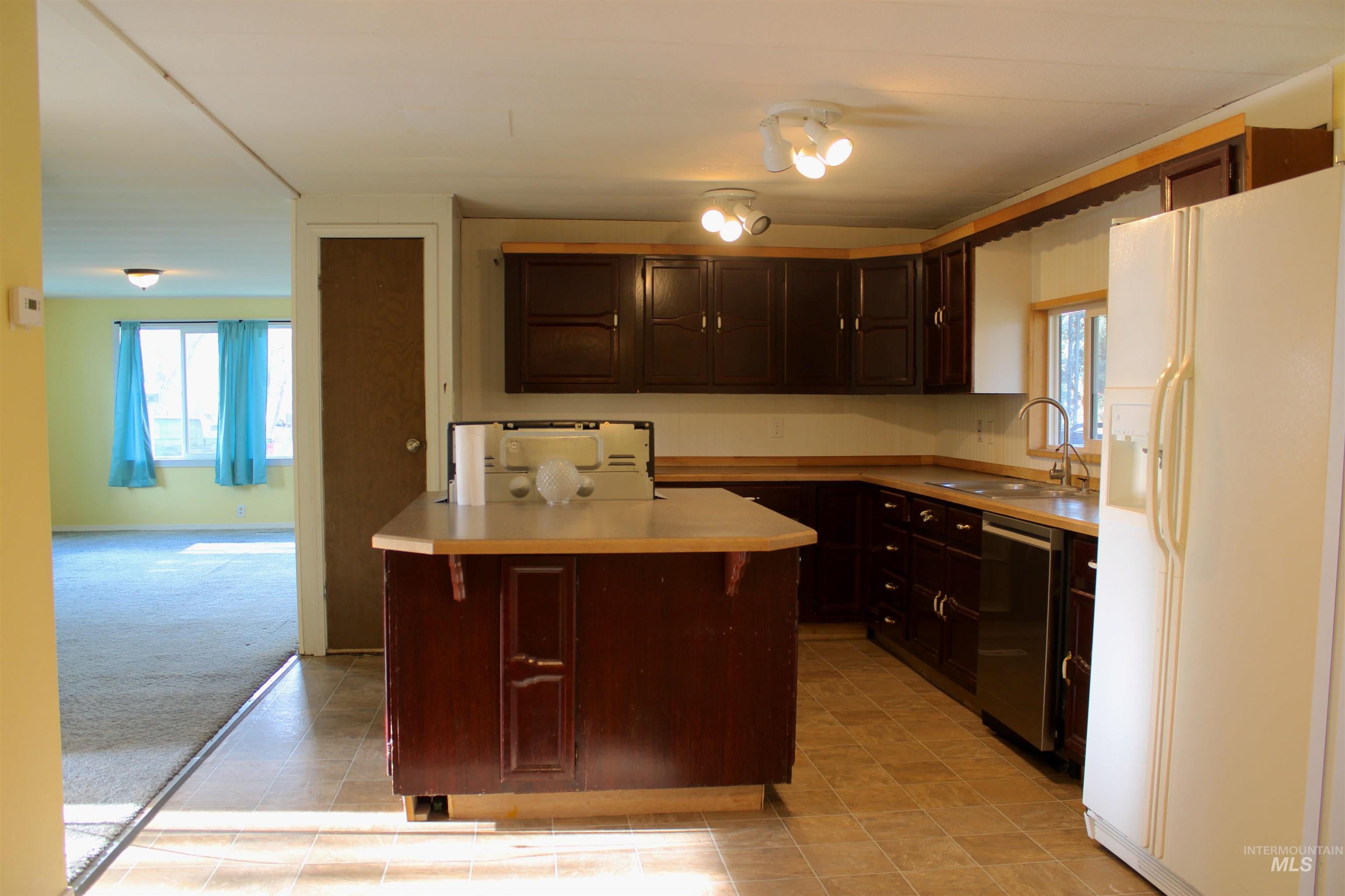 Kitchen with white refrigerator with ice dispenser, dark brown cabinets, light countertops, a kitchen island, and dishwasher