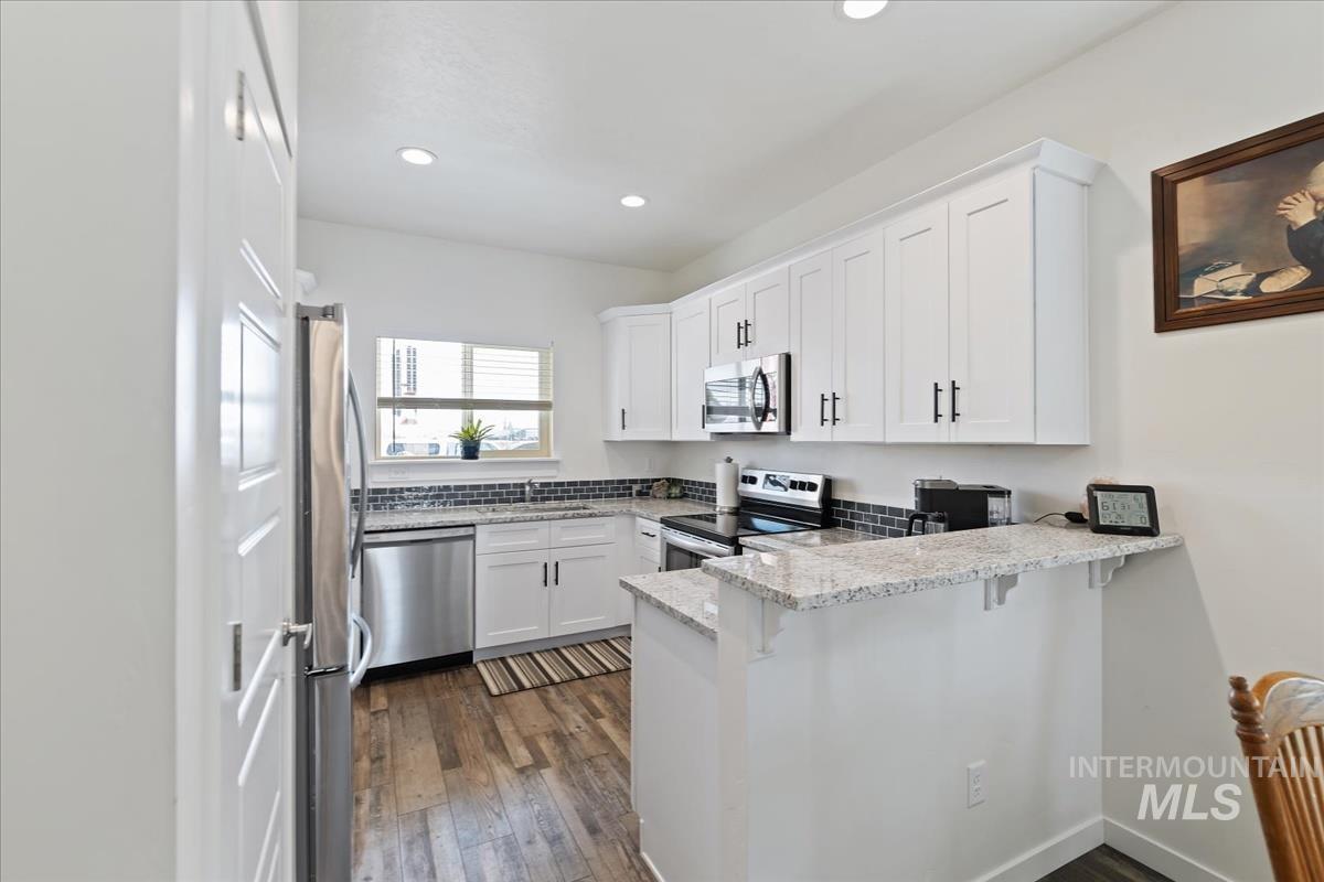 Kitchen with white cabinetry, light stone counters, a peninsula, stainless steel appliances, and a kitchen breakfast bar