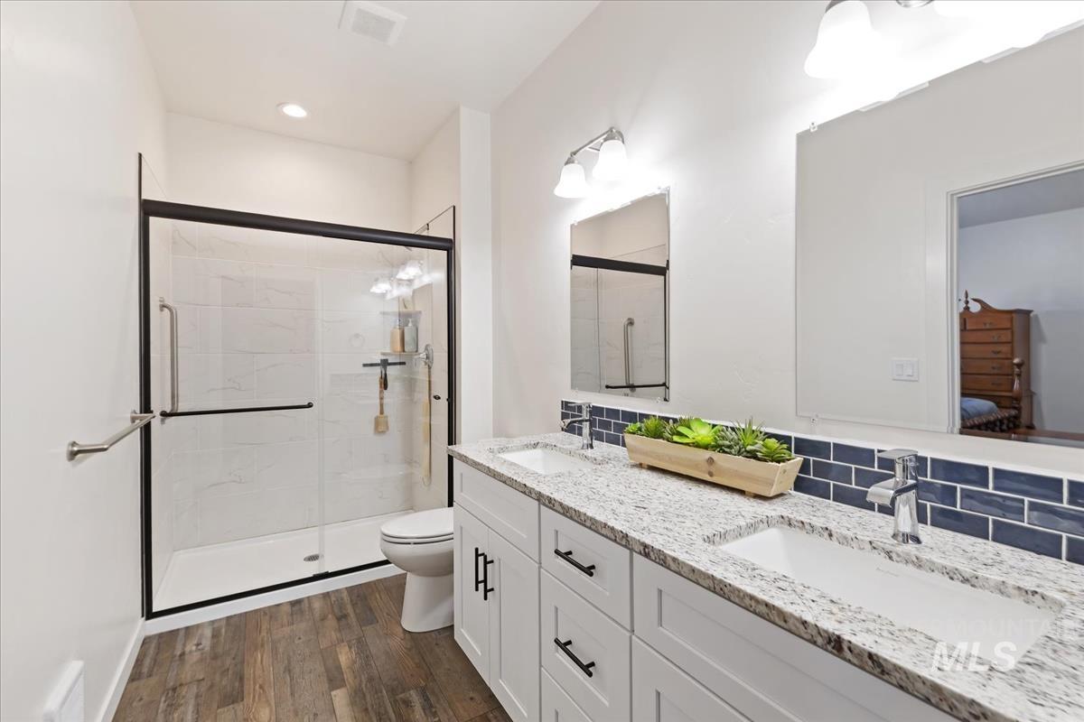 Ensuite bathroom with double vanity, dark wood-type flooring, a stall shower, and recessed lighting