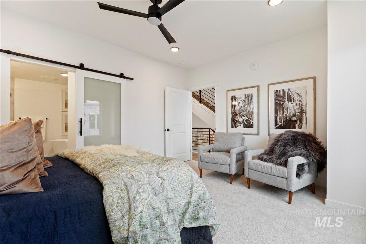 Carpeted bedroom with a barn door, connected bathroom, a ceiling fan, and recessed lighting