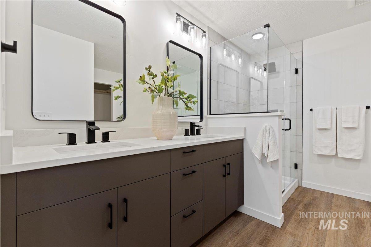 Full bathroom with double vanity, a shower stall, light wood-type flooring, and a textured ceiling