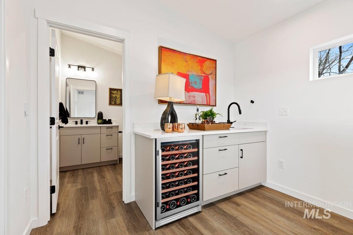 Indoor wet bar featuring beverage cooler, white cabinets, dark wood-style flooring, and light stone counters