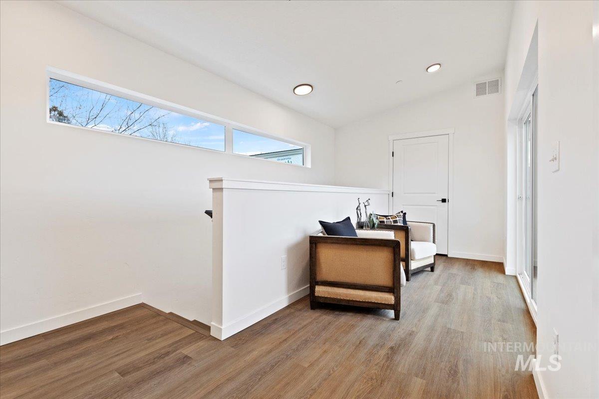 Corridor with wood finished floors, lofted ceiling, an upstairs landing, and recessed lighting