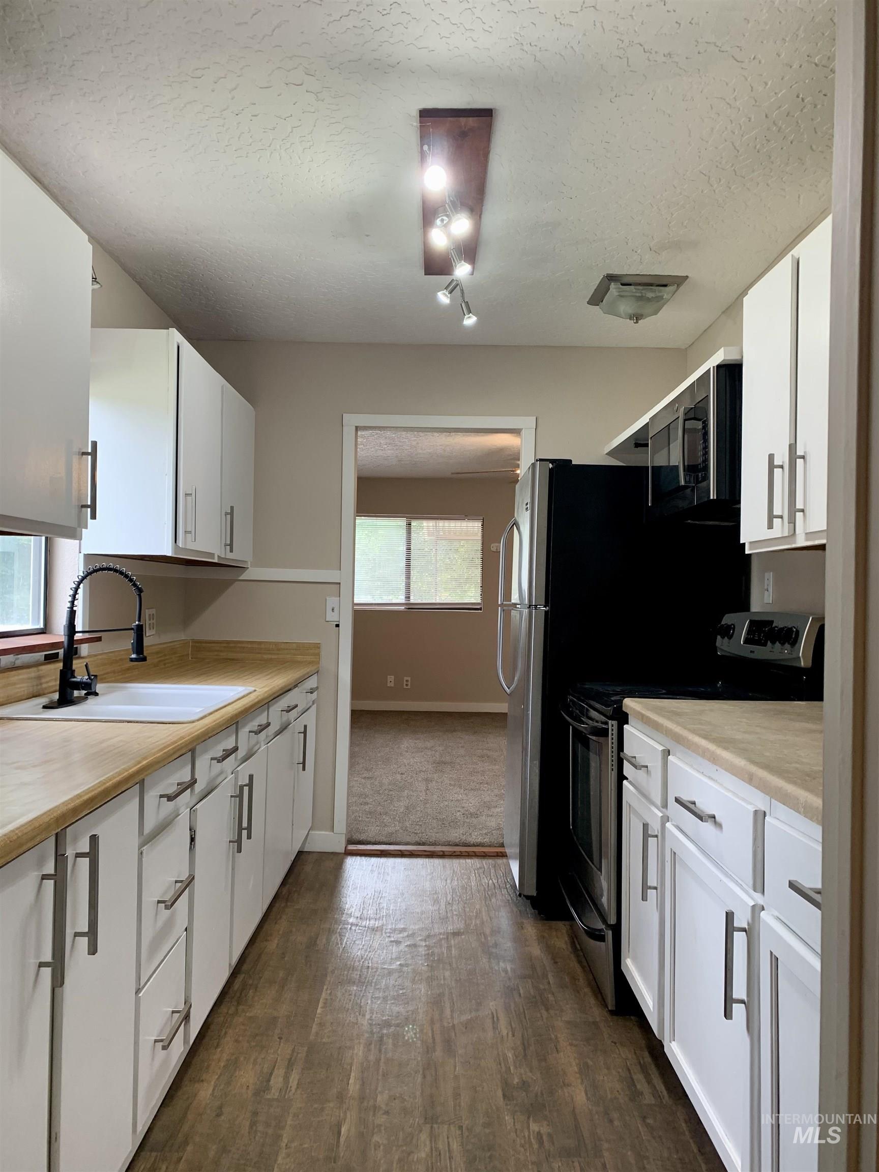 Kitchen with electric stove, light countertops, white cabinetry, and a textured ceiling