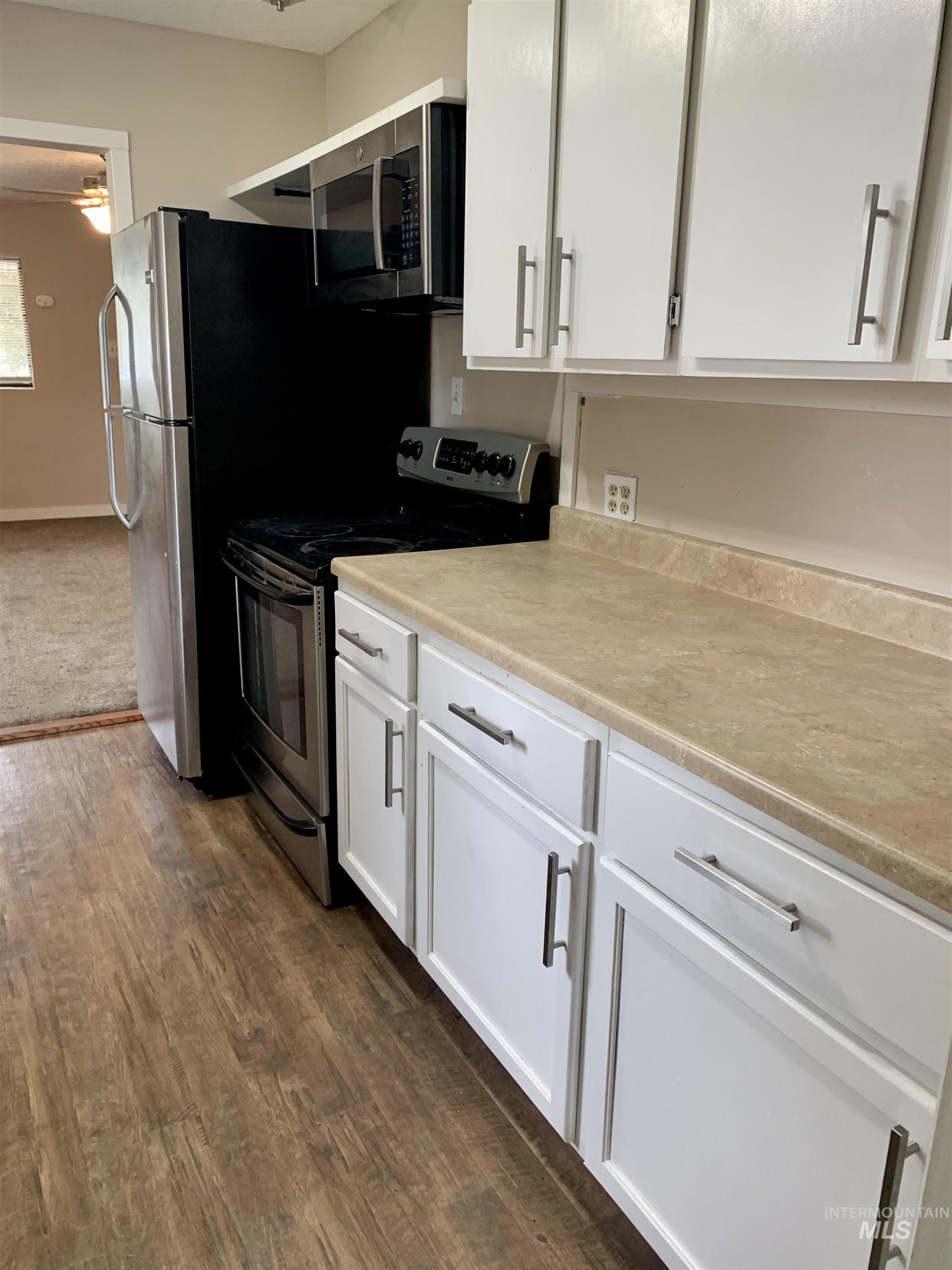 Kitchen featuring stainless steel appliances, white cabinets, light countertops, and dark wood-type flooring