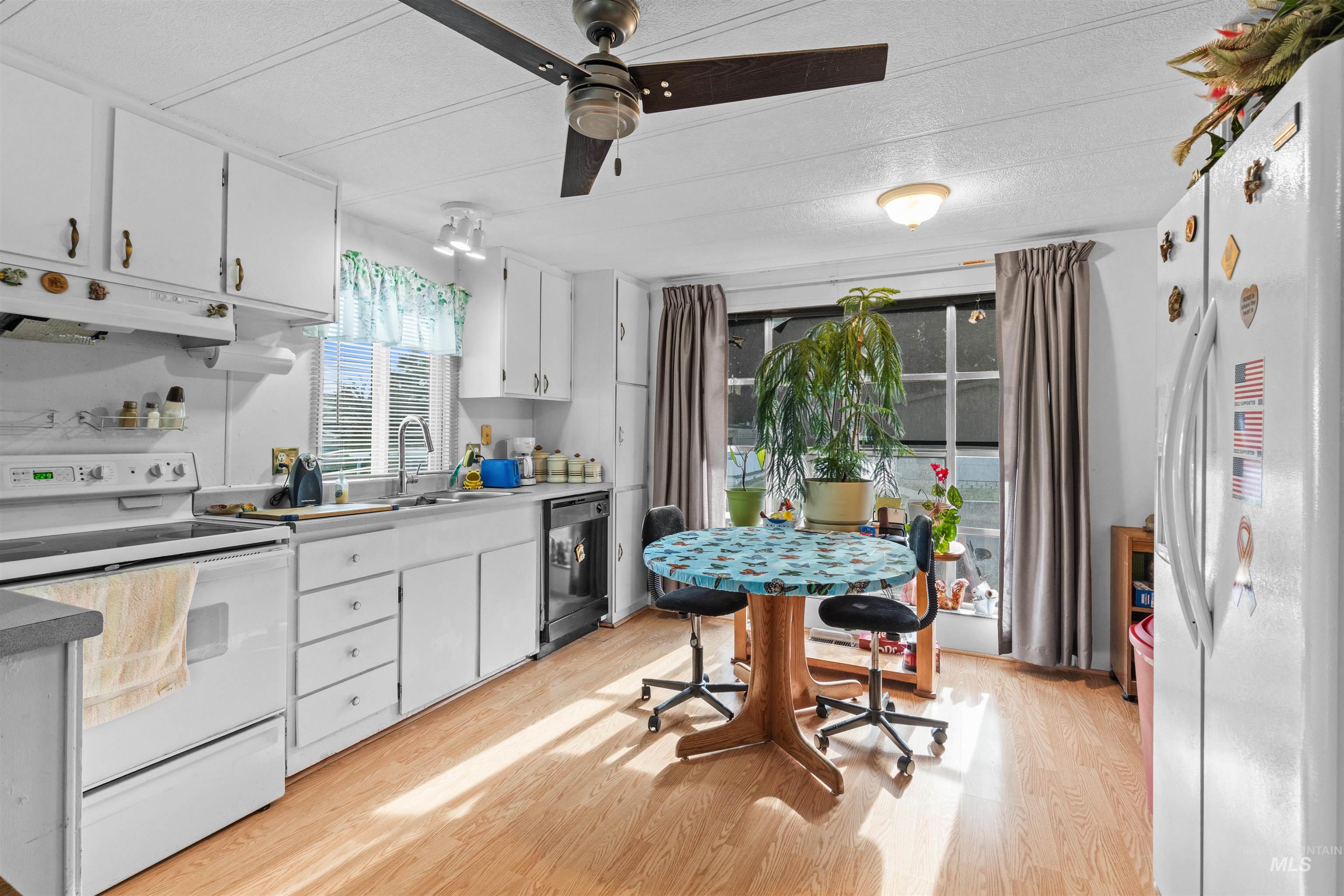 Kitchen featuring white appliances, white cabinetry, light countertops, under cabinet range hood, and a textured ceiling