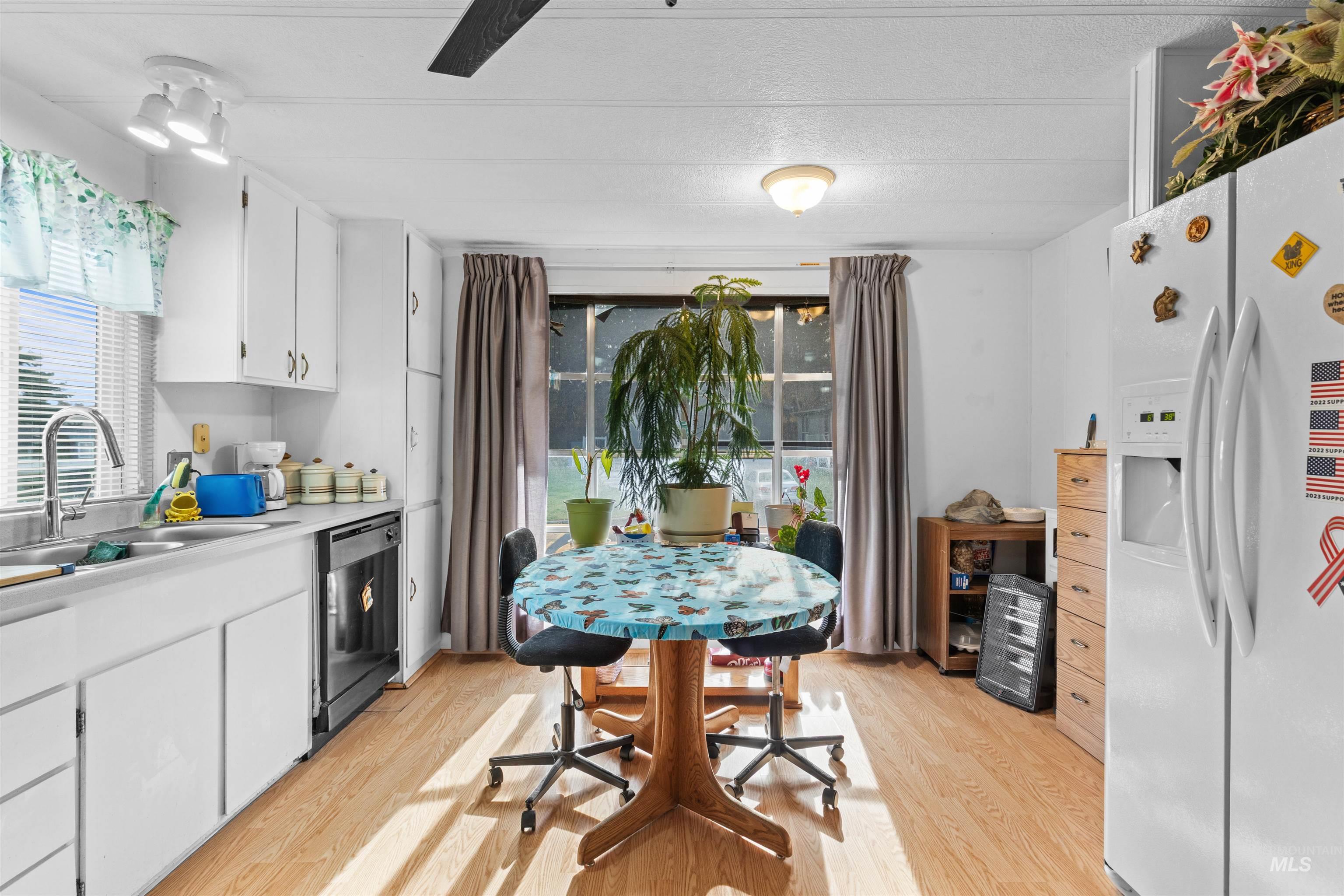 Kitchen with white fridge with ice dispenser, white cabinetry, light countertops, light wood-type flooring, and stainless steel dishwasher