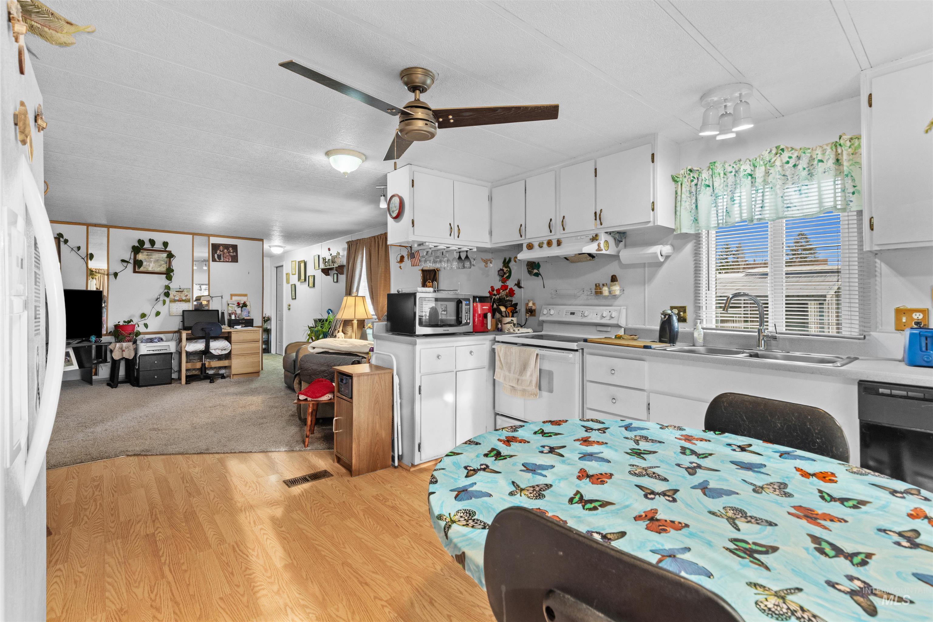 Kitchen with white cabinets, white range with electric stovetop, fridge, stainless steel microwave, and light wood-type flooring