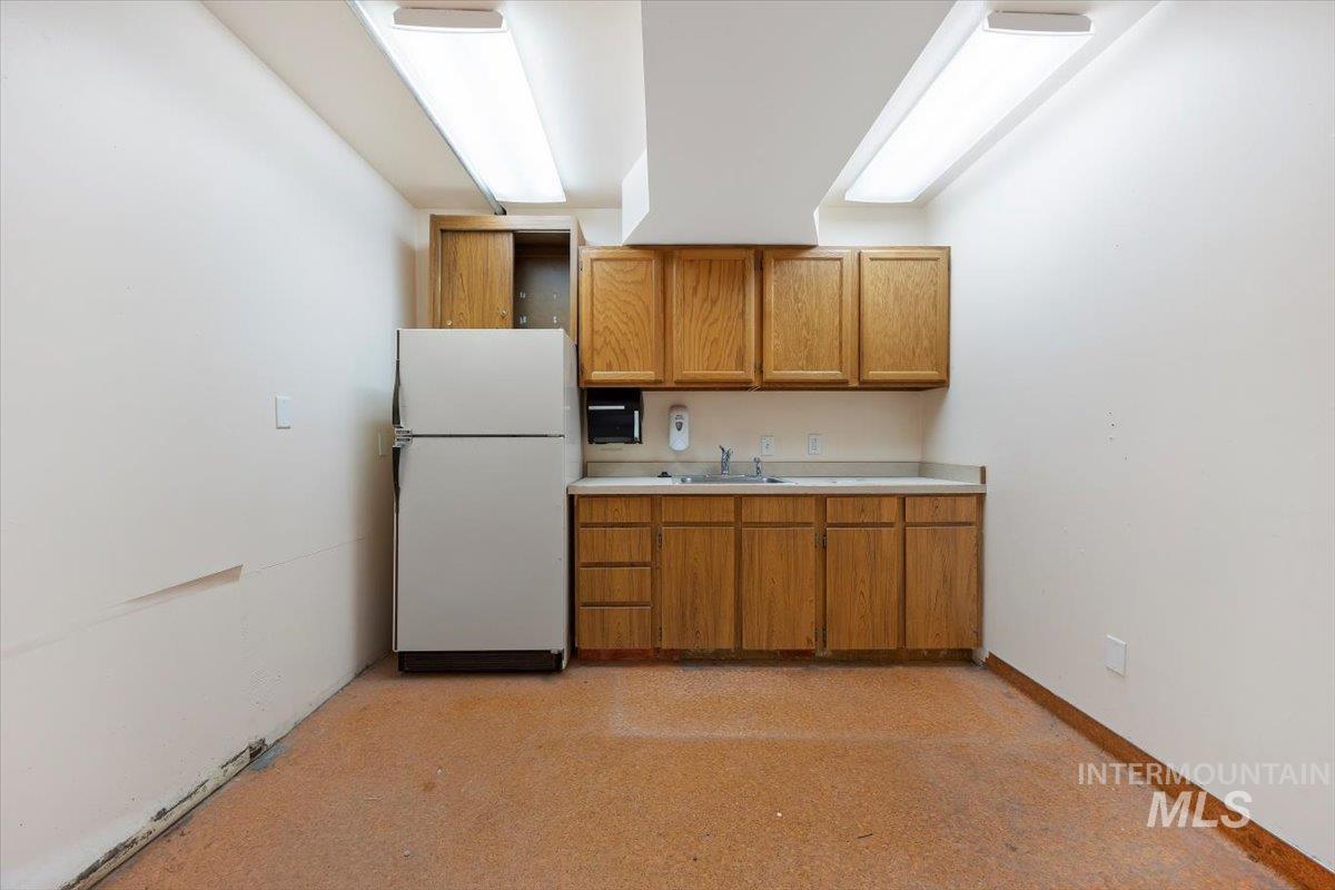 Kitchen with light countertops, freestanding refrigerator, brown cabinets, and light floors