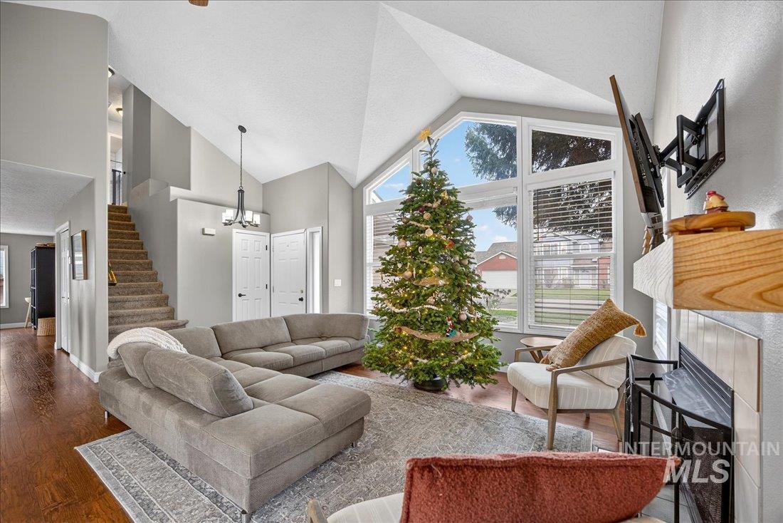 Living area featuring a fireplace, high vaulted ceiling, wood finished floors, stairway, and a chandelier