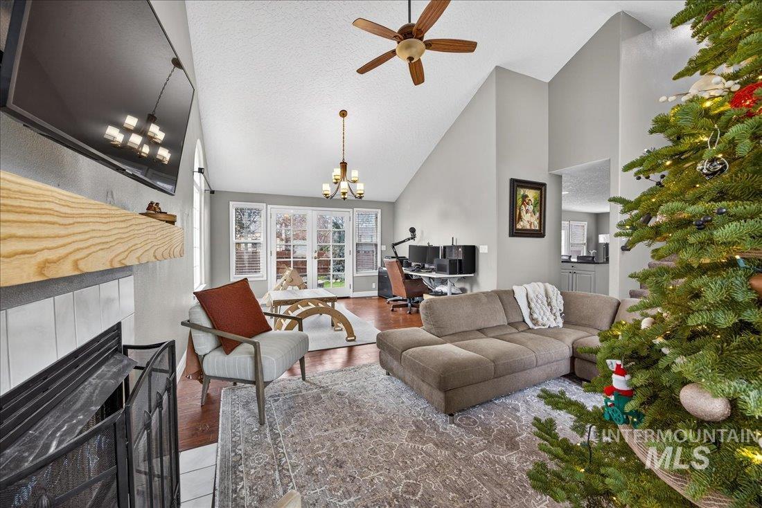 Living room with an office area, a tile fireplace, a textured ceiling, wood finished floors, and high vaulted ceiling