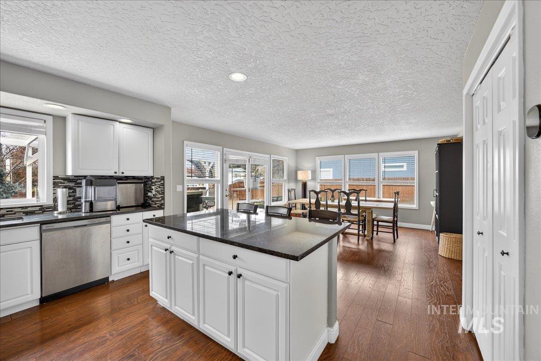 Kitchen featuring white cabinetry, dark stone counters, stainless steel dishwasher, dark wood finished floors, and a textured ceiling