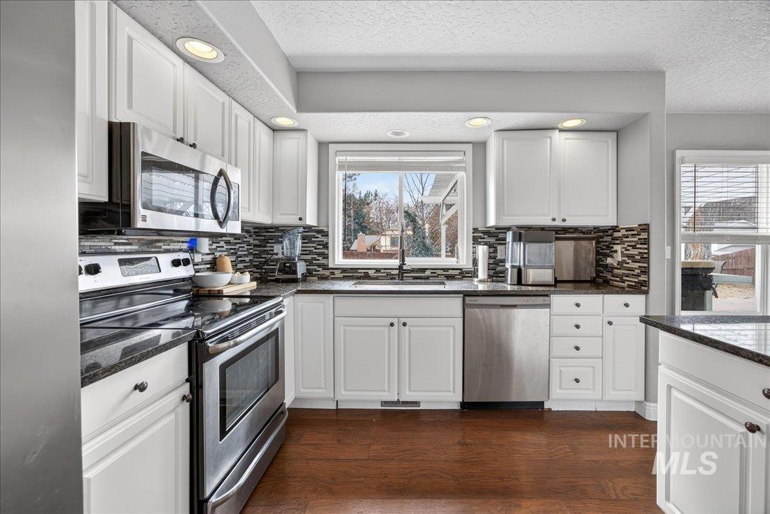 Kitchen featuring stainless steel appliances, dark stone countertops, white cabinets, dark wood finished floors, and recessed lighting
