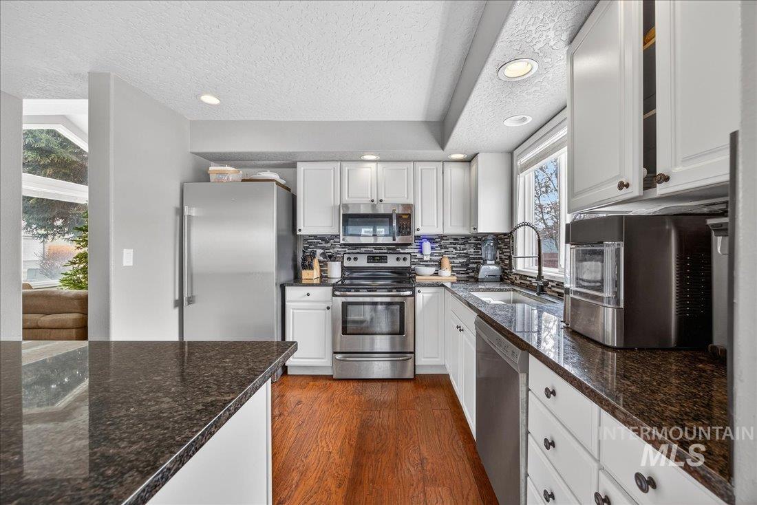 Kitchen with appliances with stainless steel finishes, dark stone countertops, white cabinets, recessed lighting, and a textured ceiling