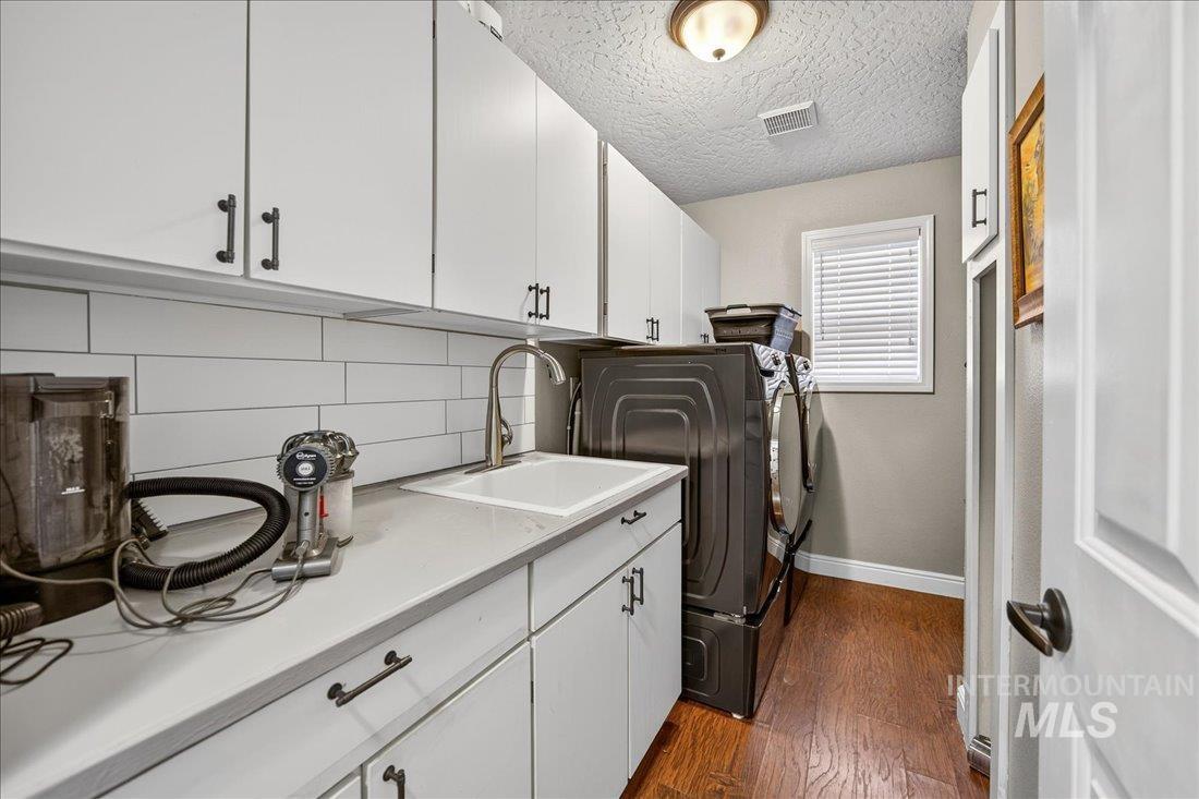 Laundry room featuring cabinet space, dark wood-type flooring, a textured ceiling, and washing machine and clothes dryer