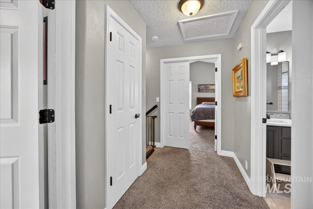 Corridor with carpet, attic access, a textured ceiling, and an upstairs landing