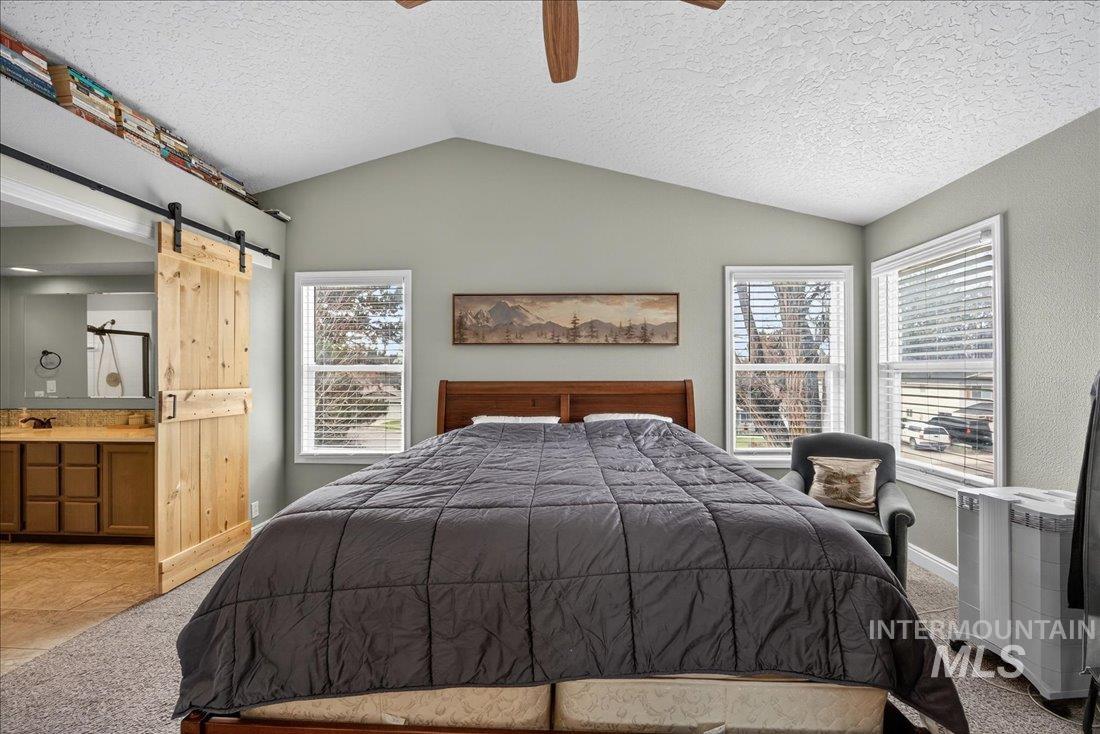 Bedroom featuring lofted ceiling, a barn door, ensuite bathroom, a textured ceiling, and a ceiling fan