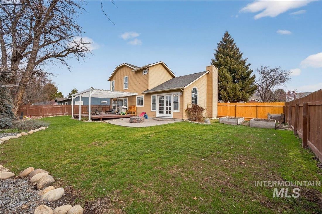 Rear view of house featuring a fenced backyard, a chimney, a fire pit, a deck, and a garden