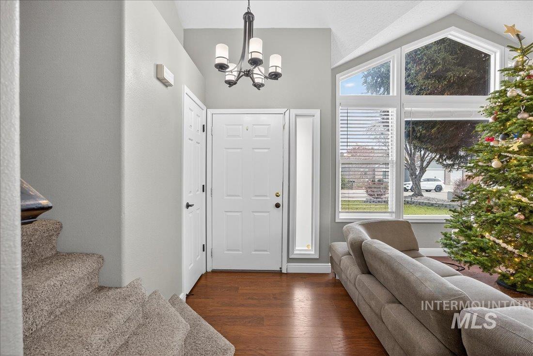 Foyer featuring lofted ceiling, dark wood-type flooring, a chandelier, and stairway