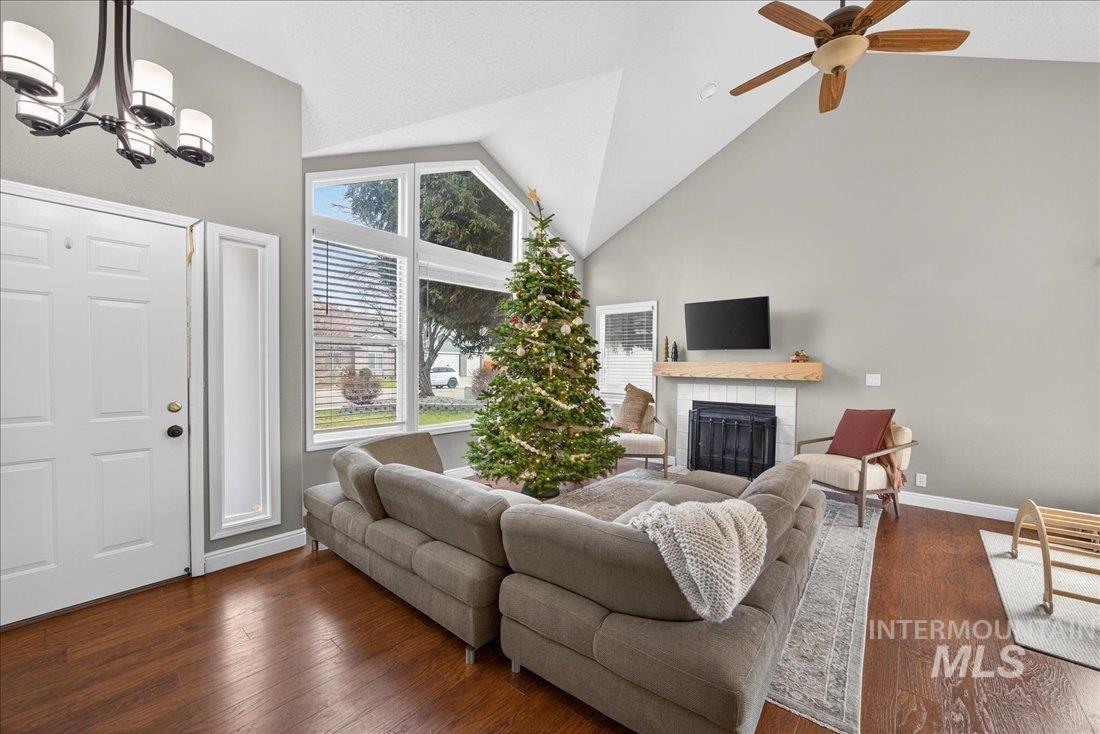 Living room featuring dark wood finished floors, a tiled fireplace, high vaulted ceiling, a chandelier, and ceiling fan